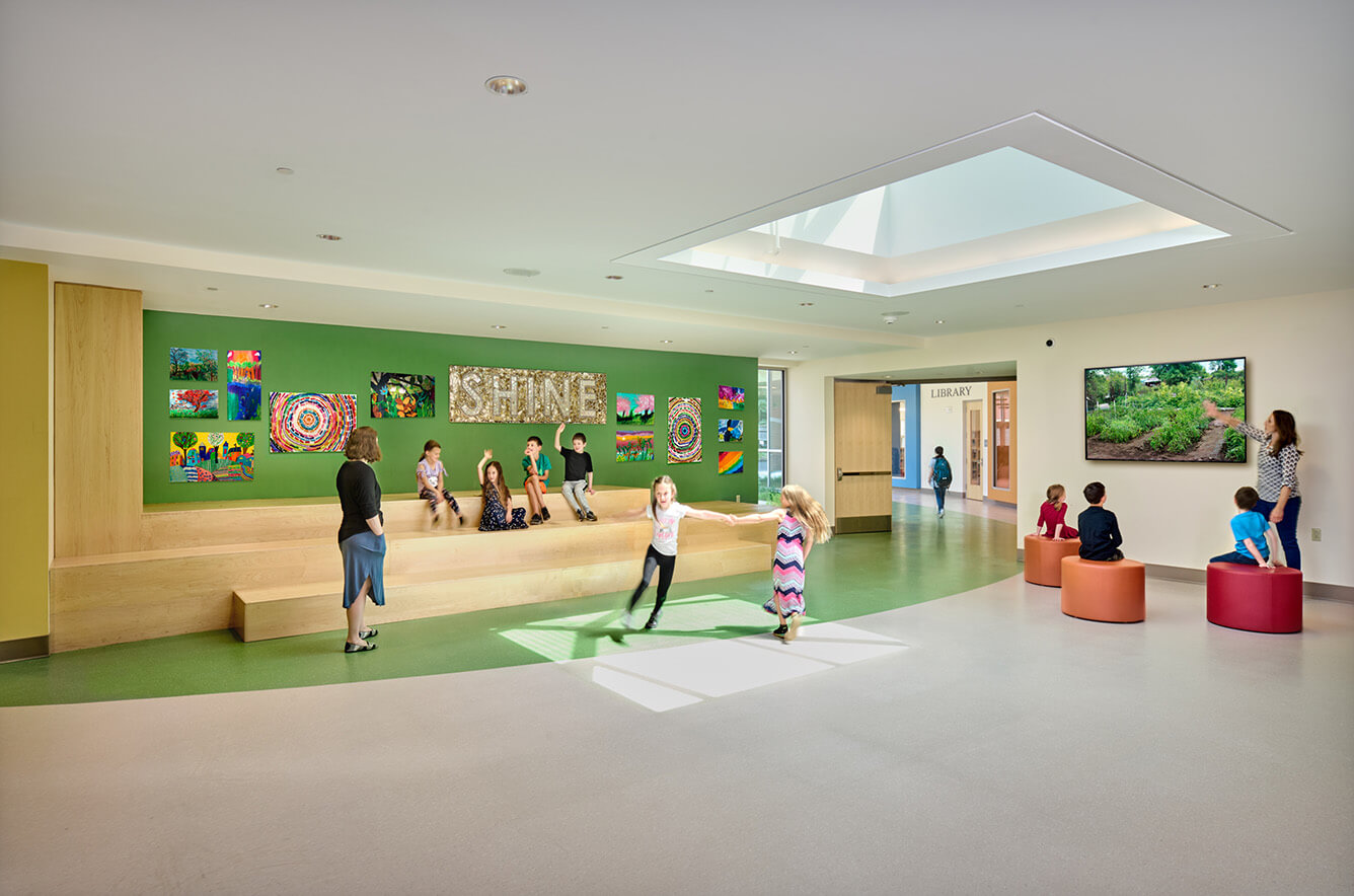 children playing in a school common room with teachers overseeing