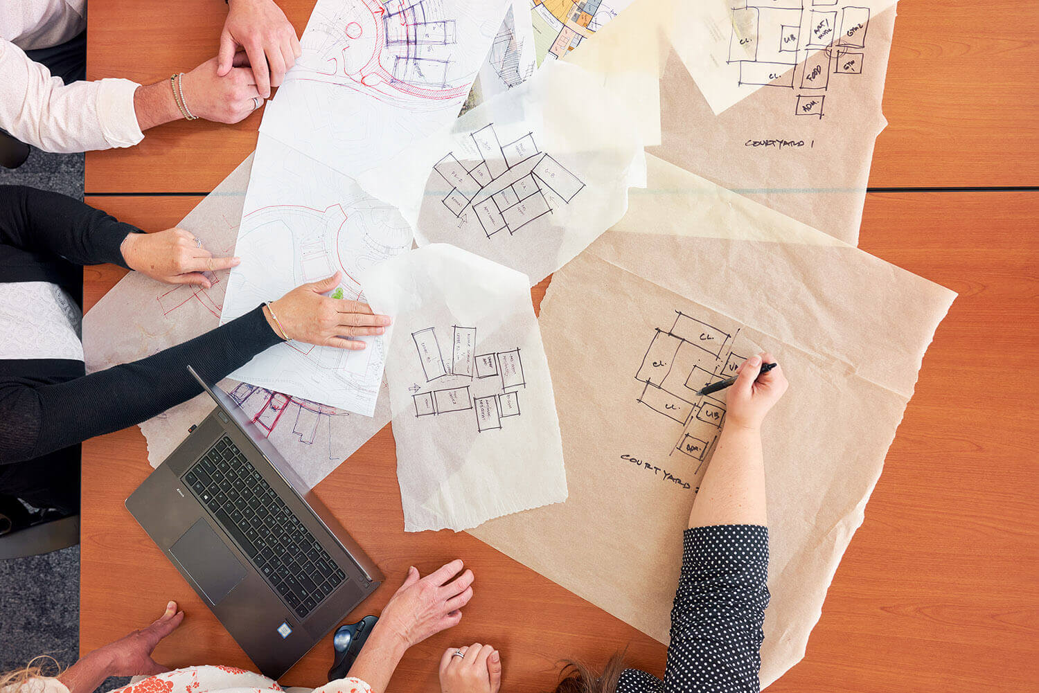 Architects' hands looking over several different blueprints